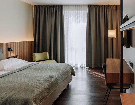 Modern hotel room with large bed, desk, chair and window with curtains and blackout curtains.