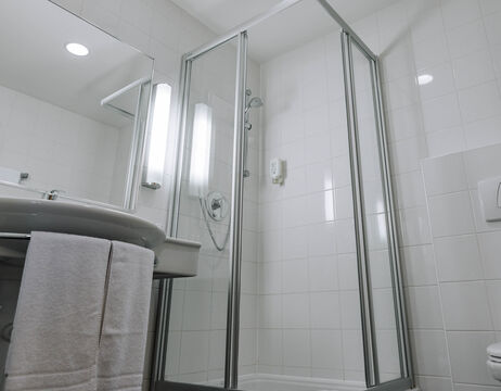 Modern bathroom with glass shower enclosure, white tiles, washbasin, mirror and towels hanging above the washbasin.