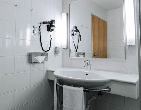 Modern bathroom with wall-mounted washbasin, mirror, hairdryer, towel and bright ceiling lighting.