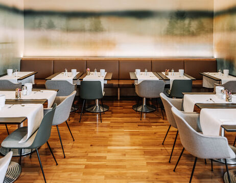 Modernes Restaurant mit hellem Holzfußboden, grauen Stühlen und weiß gedeckten Tischen mit Gewürzen.