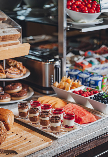 Mixed breakfast buffet with pastries, yogurt, fruit, bread and layered dessert cups on a counter.