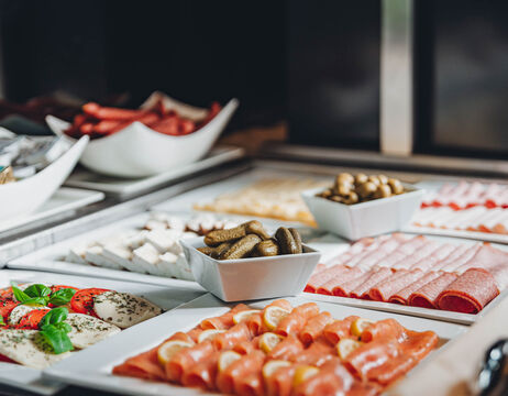 Ein Buffettisch mit verschiedenen Wurst- und Käsesorten und kleinen Gurken auf weißen Tellern.