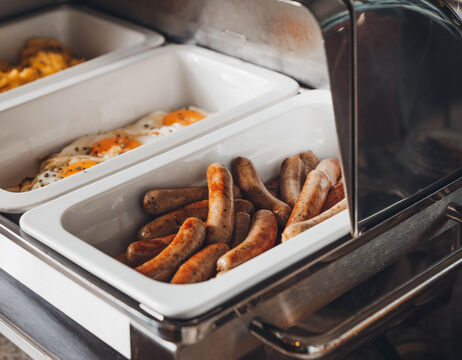 Tablett mit Brühwürsten und Tablett mit Spiegeleiern in einer Servierstation in Buffetform.