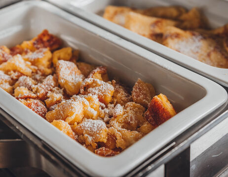 Goldbraun gebackene, mit Puderzucker bestäubte Dessertstücke in einer weißen Servierschale.