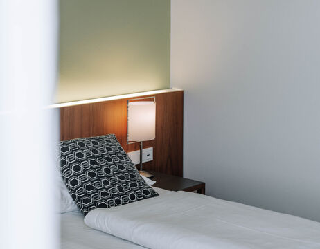 A neatly made bed with a patterned pillow and a lighted lamp on a bedside table in a modern room.
