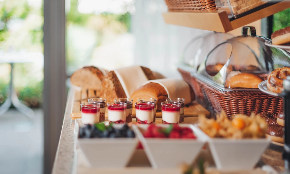 Breakfast buffet with various types of bread, pastries, yogurt parfaits and bowls of fresh berries on a counter.