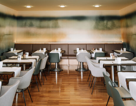 Modernes, leeres Café mit grauen Stühlen, weißen Tischen und einer verschwommenen Landschaftsmalerei an der Rückwand.