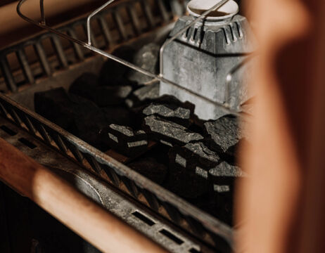Close-up of a sauna heater with dark sauna stones and a metal grille in warm, soft lighting.