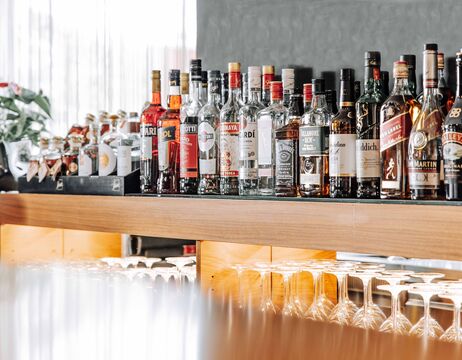 Verschiedene Schnapsflaschen sind auf einem Bartresen aufgereiht, darunter befinden sich Glaswaren.