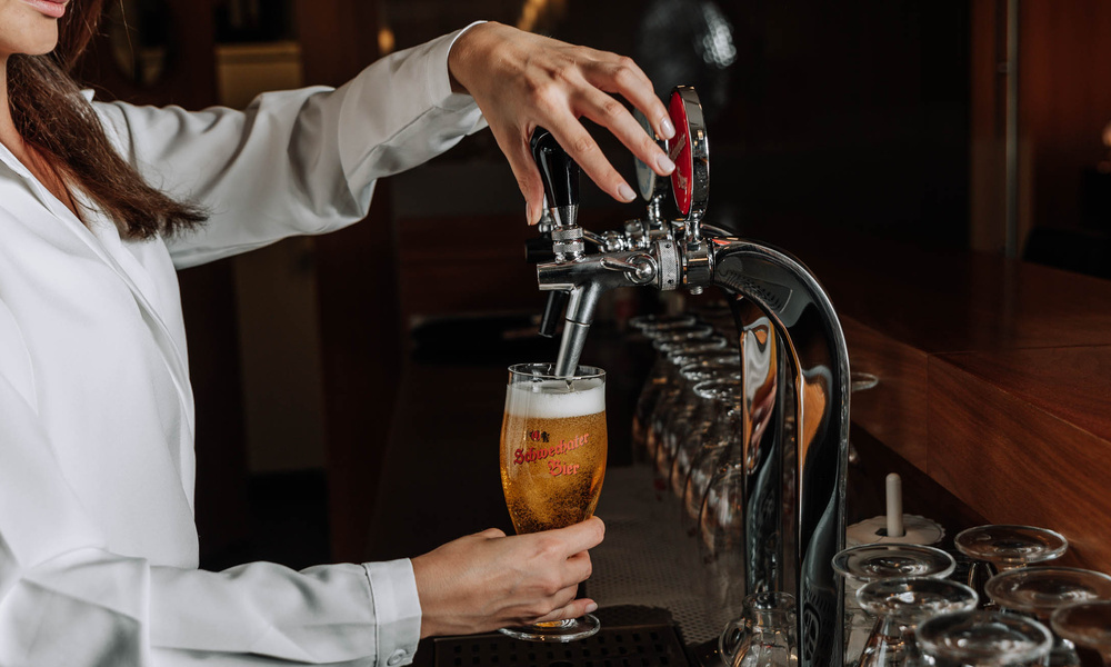 A person pours draught beer from a tap into a glass at a bar counter.