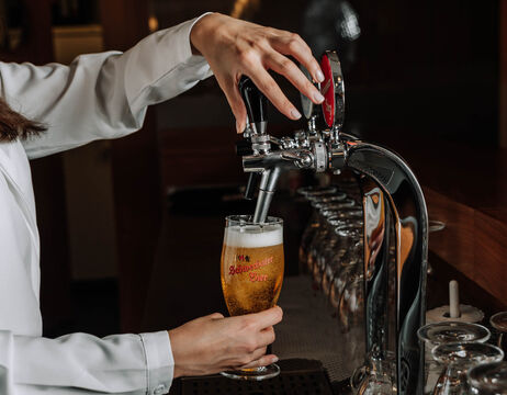 A person pours draught beer from a tap into a glass at a bar counter.
