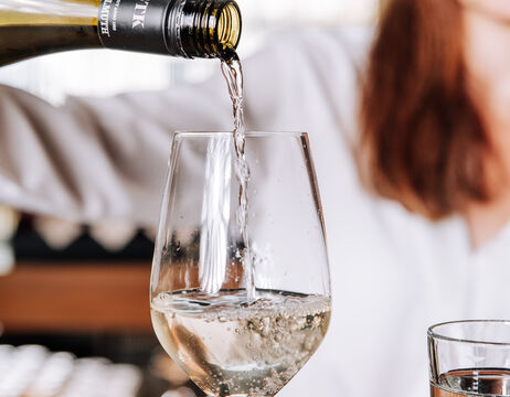 White wine is poured into a glass and a person wearing a white shirt can be seen in the background.
