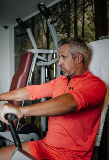 A man in a bright orange outfit uses fitness equipment in a fitness center.