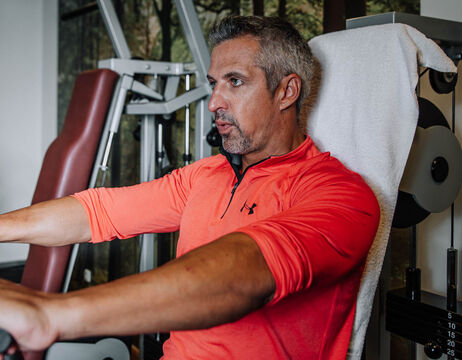 A man in an orange shirt uses a weight machine in a gym and concentrates on his workout.