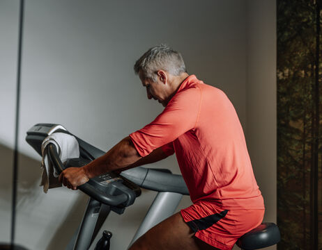 A man in red workout clothes rides a stationary bike indoors and concentrates on his training.