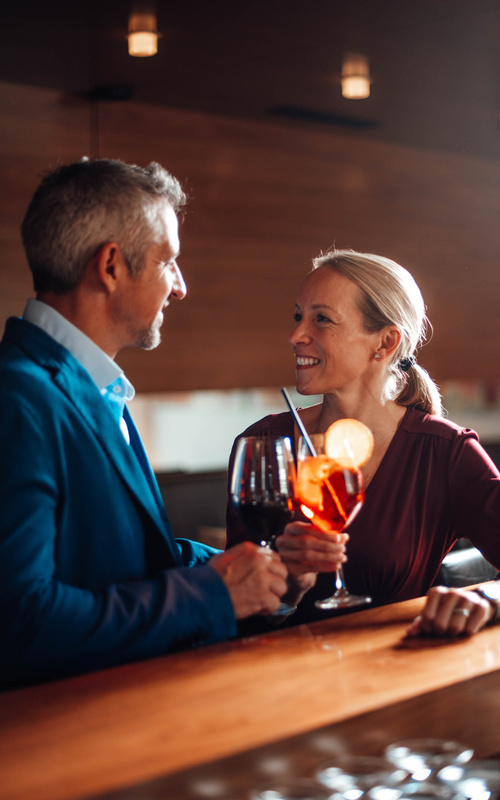 A smiling man and a smiling woman clink glasses at a bar and enjoy drinks together in a warm environment.