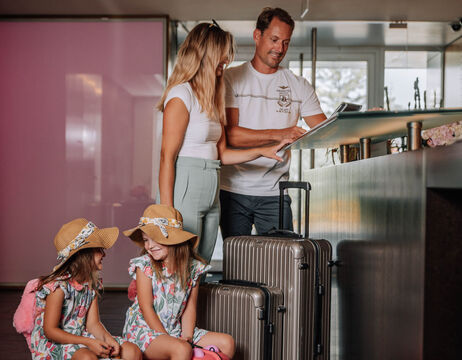 Eine Familie mit zwei kleinen Mädchen und Gepäck checkt an der Rezeption eines Hotels ein.