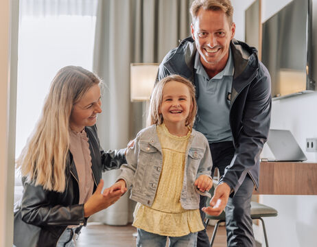 Lächelnde Familie mit einem jungen Mädchen, die zusammen in einem modernen, gut beleuchteten Raum stehen.