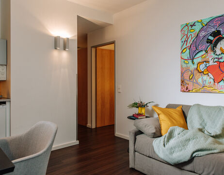 Modernes Wohnzimmer mit grauem Sofa, farbenfroher Kunst an der Wand und einer kuscheligen Decke und Kissen.