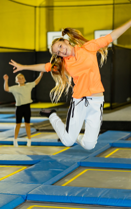 Lächelndes Mädchen, das auf einem Trampolin in einem Haus springt, mit einer anderen Person im Hintergrund.