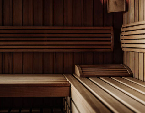 Empty wooden sauna with benches and a headrest, softly illuminated by warm light.